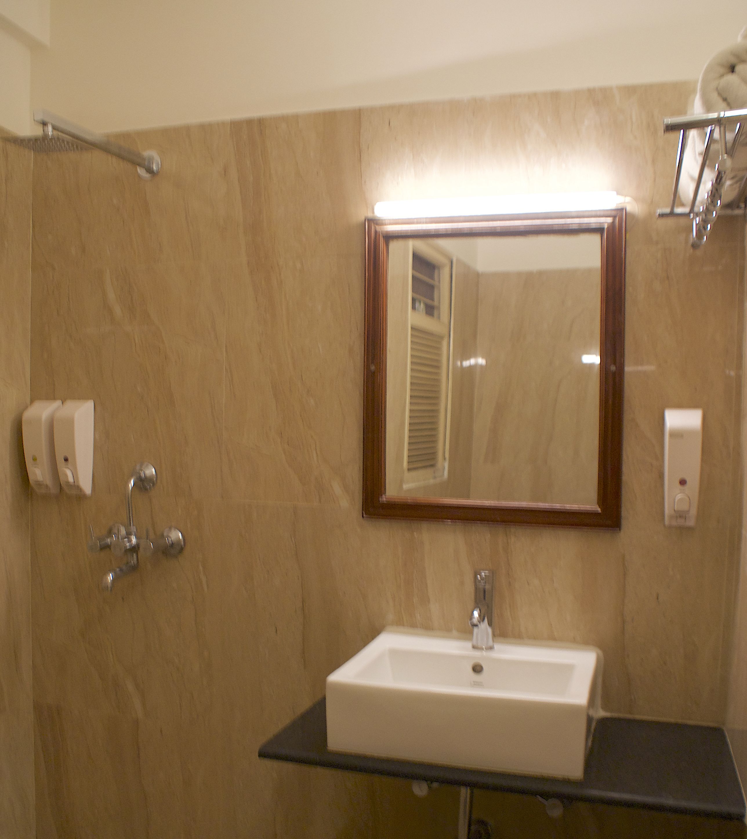 Un baño con un lavamanos blanco, un espejo y un perchero para toallas.