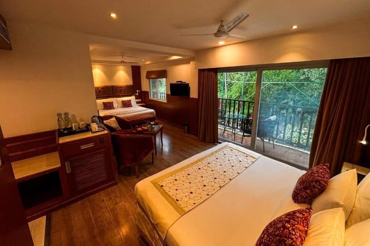 A hotel room with a large bed, a desk, a chair, and a balcony with a view of greenery.