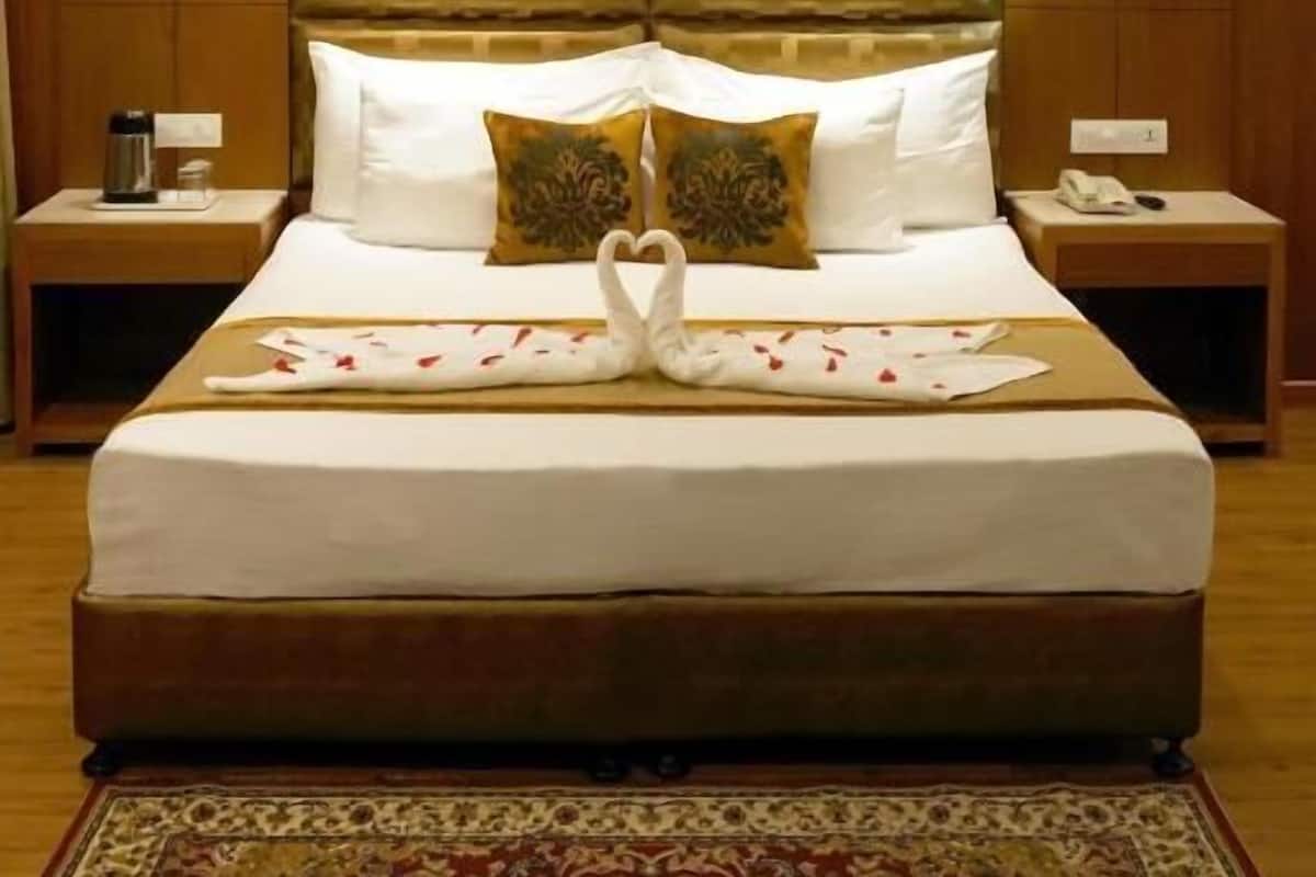 A hotel room with a large bed, wooden headboard, two bedside tables, a ceiling fan, and a patterned rug.