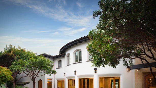 A white building with arched windows and a tiled roof, surrounded by lush greenery and a paved courtyard. - El Colibri Hotel & Spa (Cambria)