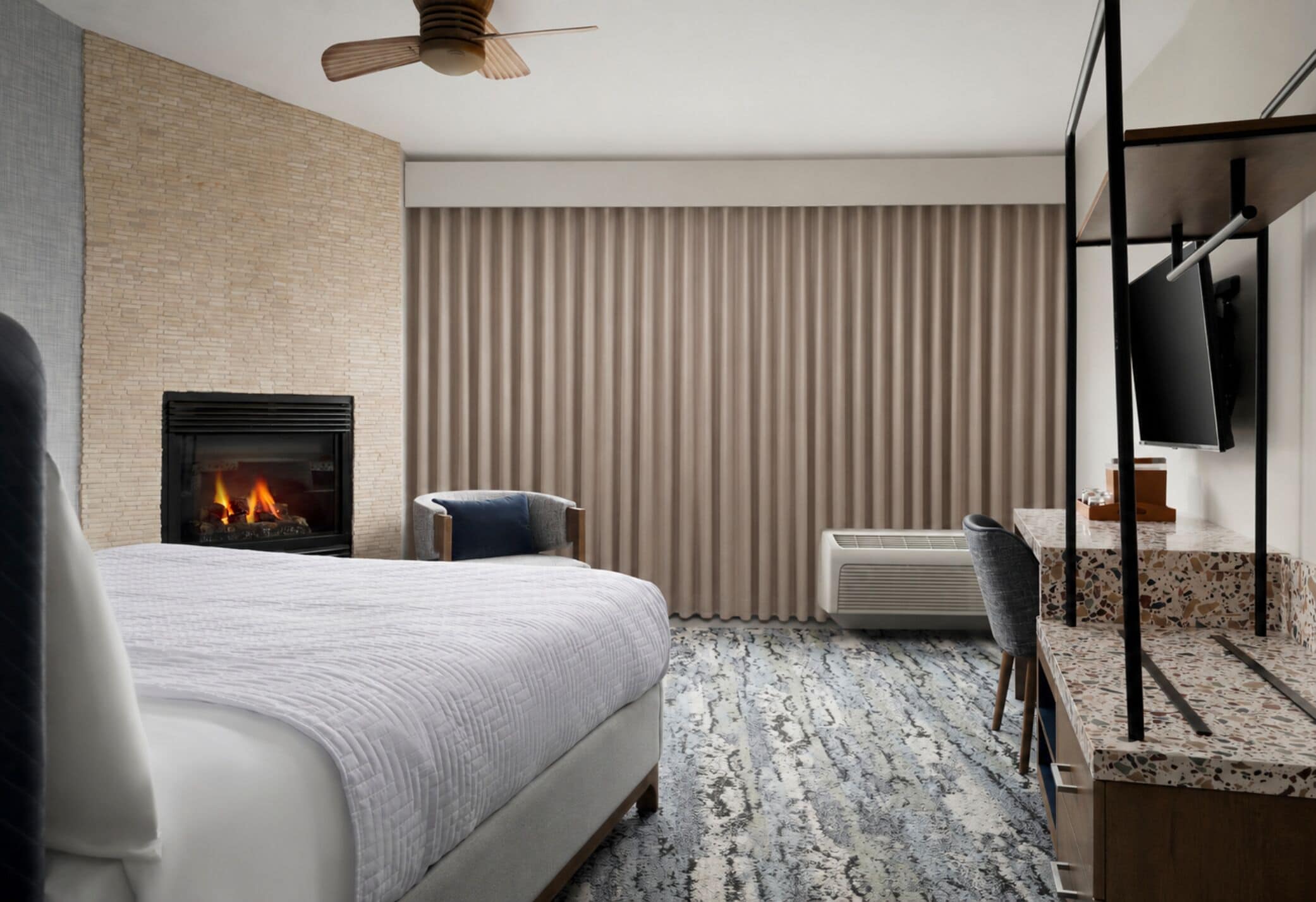 A modern hotel room with a large bed, a fireplace, a television, and a seating area.