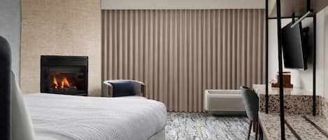 A modern hotel room with a large bed, a fireplace, a television, and a seating area.