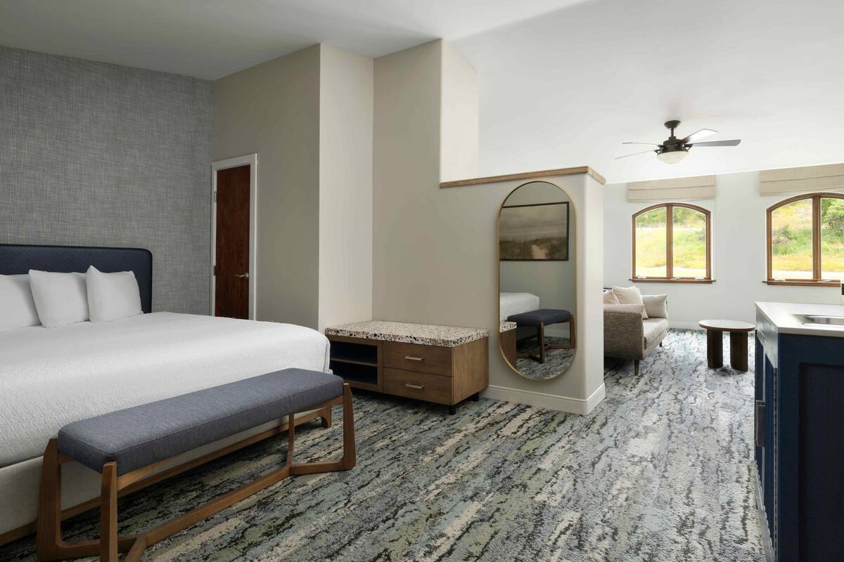 A bedroom with a bed, a bench, a dresser, a mirror, and a ceiling fan.