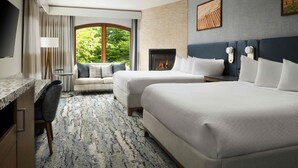 A hotel room with two beds, a desk, a chair, a fireplace, and a large window with a view of greenery. - El Colibri Hotel & Spa (Cambria)