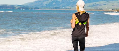 A person walking on a beach with a view of the ocean and distant hills.