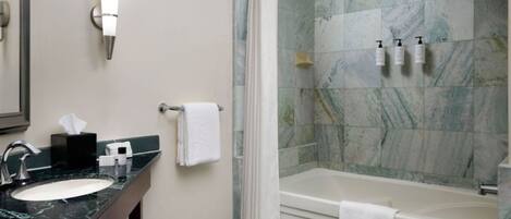 A bathroom with a marble sink, a bathtub, and a shower curtain.