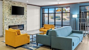 A modern living room with a stone wall, a flat-screen TV, a fireplace, and large windows offering a view of the street. - Comfort Suites Simpsonville - Greenville (Simpsonville)
