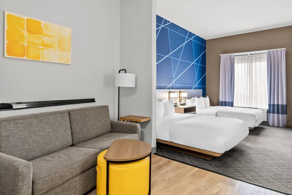 A hotel room with a sofa, a small table, a bed, a nightstand, and a wall with a geometric pattern.