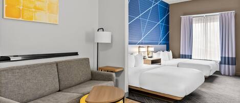 A hotel room with a sofa, a small table, a bed, a nightstand, and a wall with a geometric pattern.