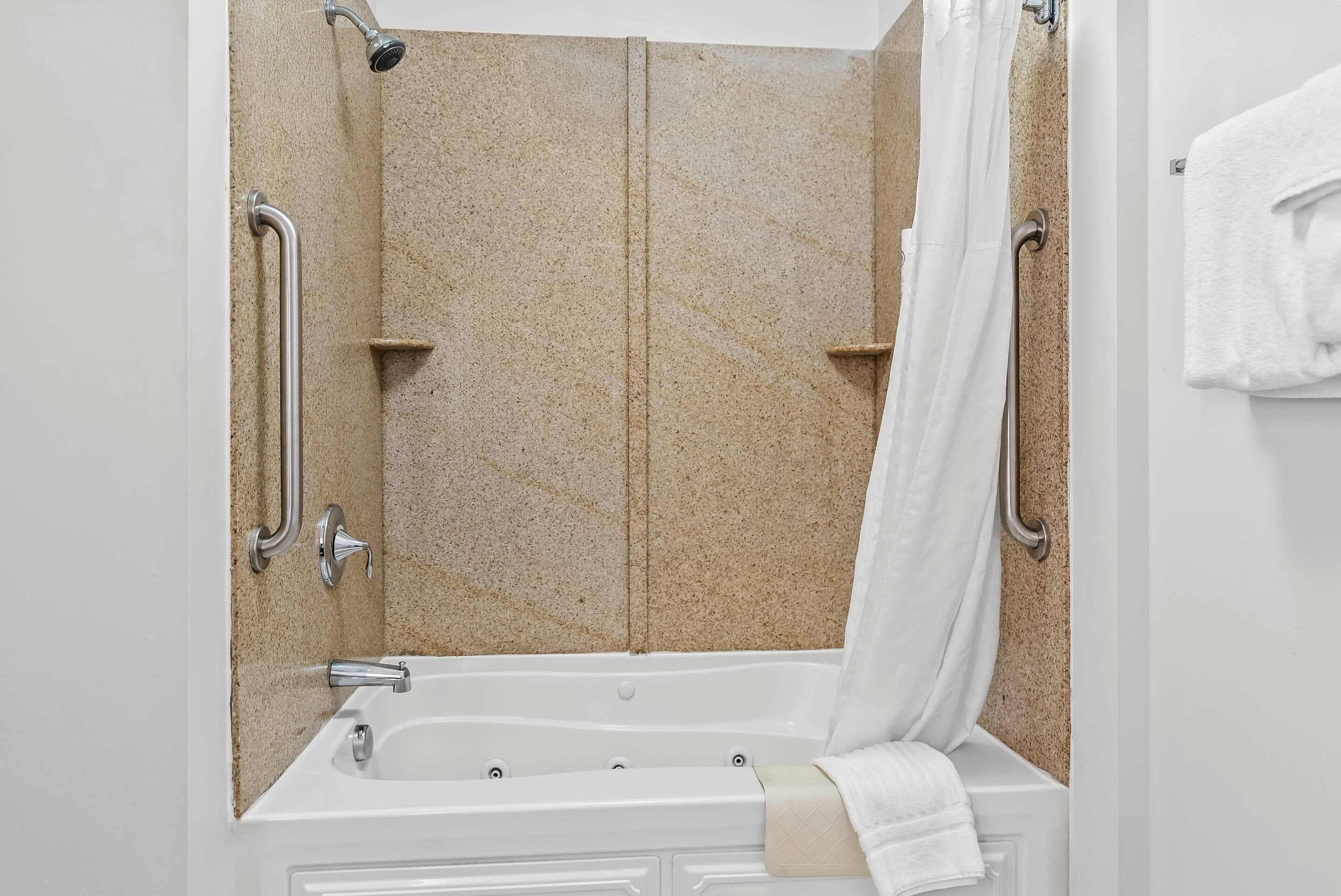 A bathroom with a bathtub, shower, and grab bars.