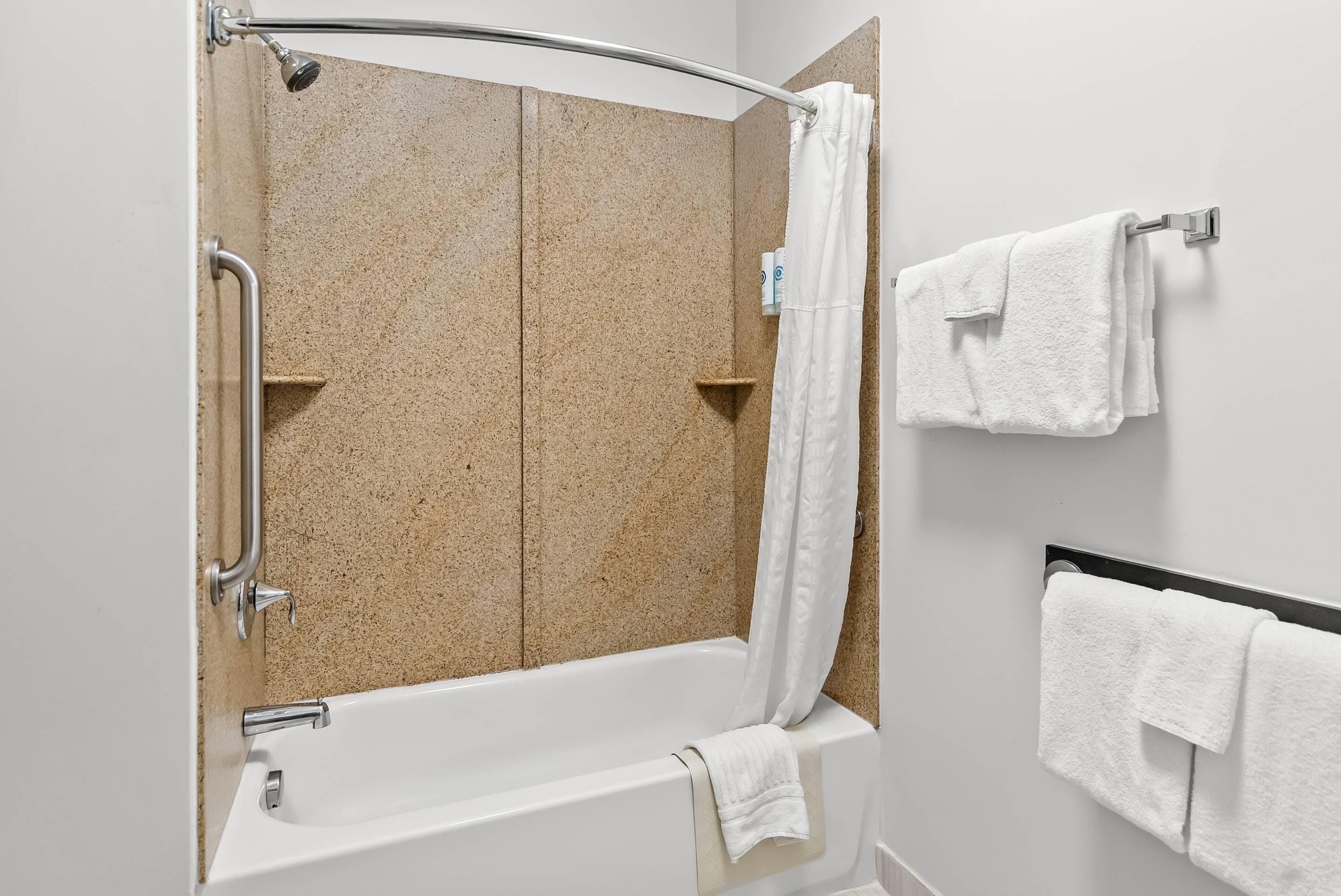 Un baño moderno con una bañera independiente, una ducha con puerta de vidrio curvada y dos toallas colgadas en un toallero de pared.