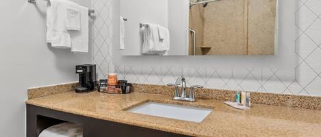 A bathroom with a sink, mirror, towel rack, and a shower area.