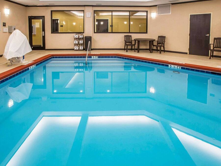 Una piscina interior limpia con borde de azulejos, un banco cubierto y una pequeña mesa con sillas.