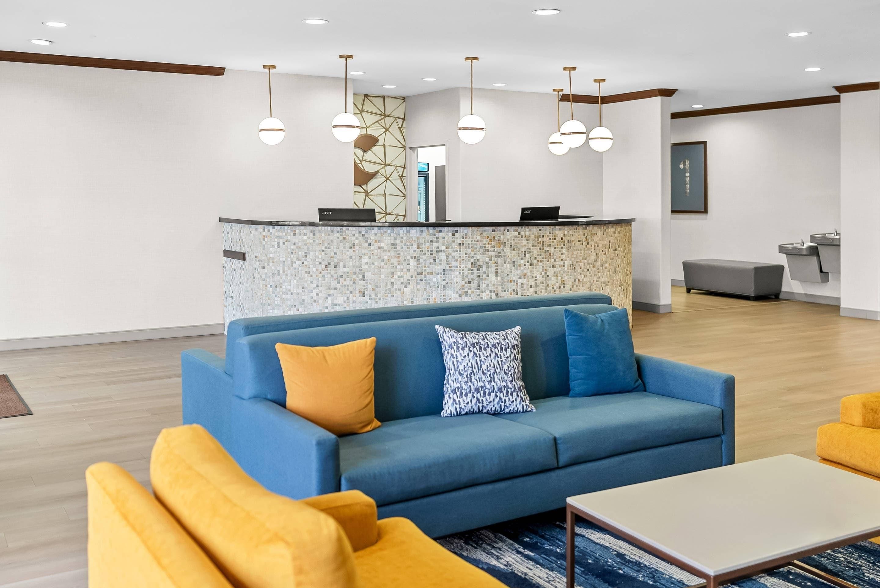A modern lobby with a blue sofa, yellow armchairs, and a reception desk with a mosaic backsplash.