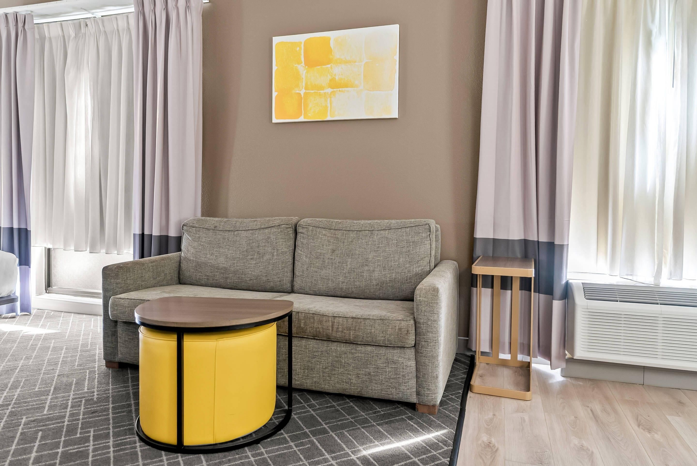 A modern living room with a grey sofa, a yellow side table, and a large abstract painting on the wall.