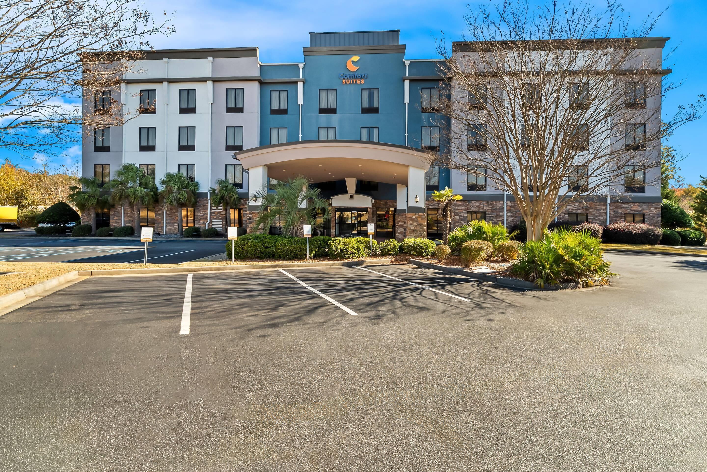 A hotel with a modern design, featuring a central entrance with a canopy, multiple floors, and a parking lot with marked spaces.