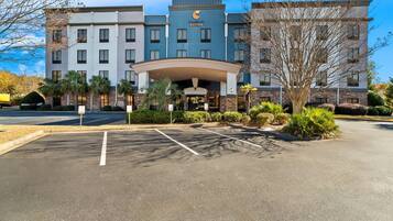 A hotel with a modern design, featuring a central entrance with a canopy, multiple floors, and a parking lot with marked spaces.