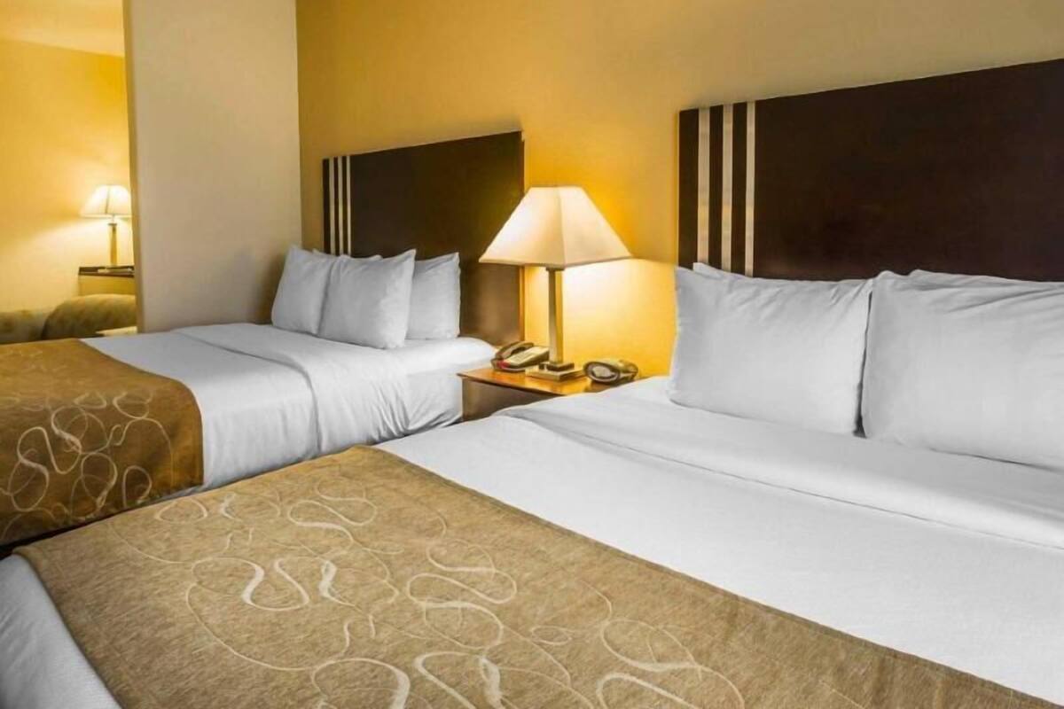 A hotel room with two beds, a bedside table with a lamp, and a telephone.