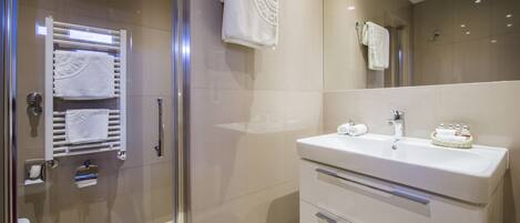 A modern bathroom with a glass shower enclosure, a white sink with a basket of toiletries, and a towel rack with multiple towels.