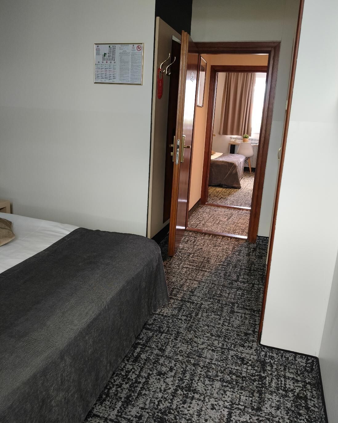Een hotelkamer met een bed, een bureau en een stoel. Er is een deur die naar een andere kamer leidt.