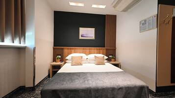 Habitación de hotel con una cama, dos mesitas de noche, un velador, un cuadro en la pared y una ventana con cortinas.