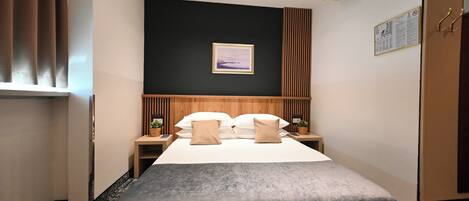 A hotel room with a bed, two bedside tables, a nightstand, a wall-mounted picture, and a window with curtains.