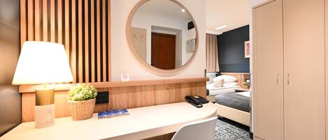 A hotel room with a desk, chair, bed, wardrobe, and a round mirror.