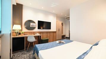 A hotel room with a bed, desk, chair, TV, and wardrobe.