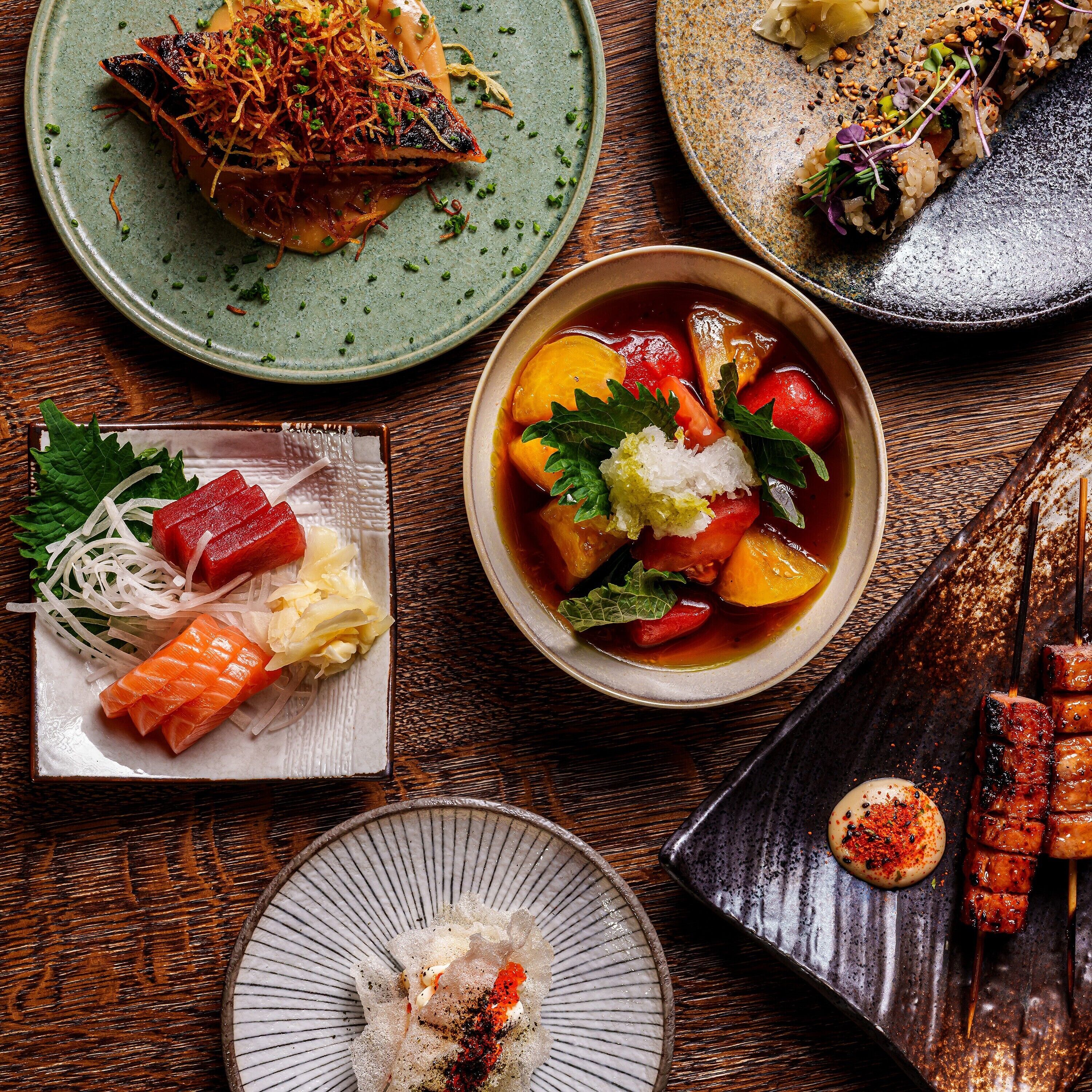 A variety of Japanese dishes including sushi, sashimi, and a bowl of soup with vegetables.