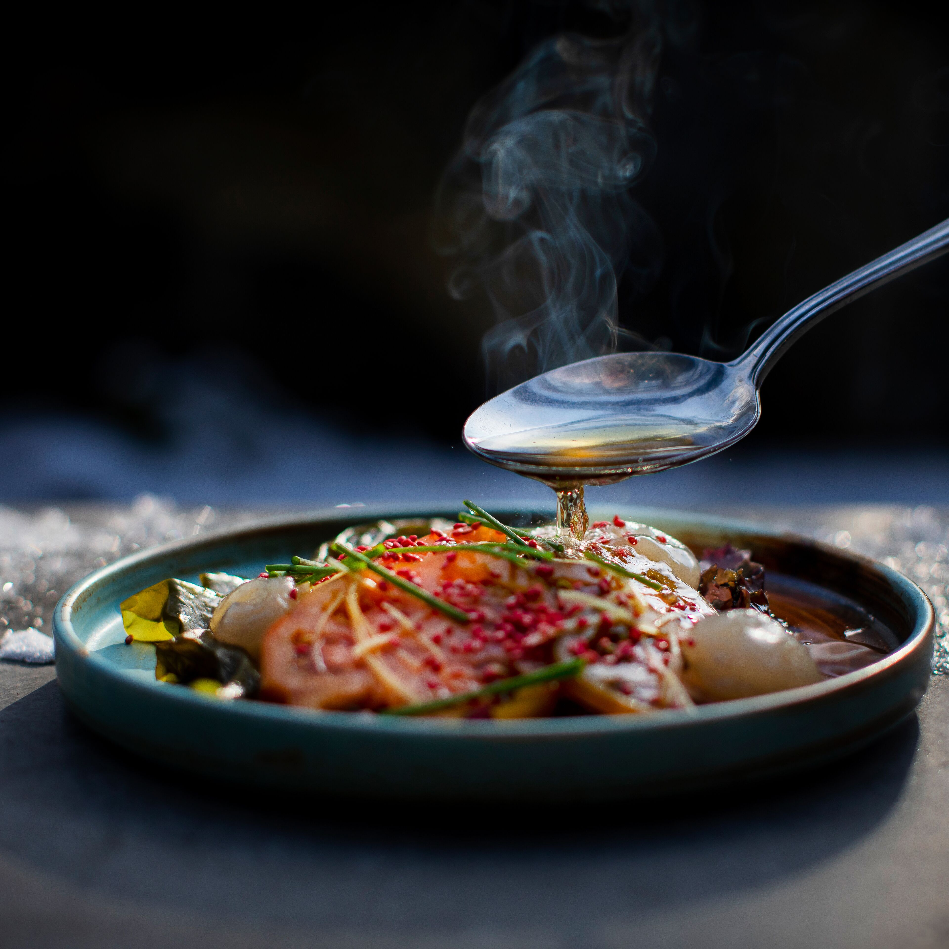 A spoonful of food being lifted from a dish with steam rising, indicating hot food.