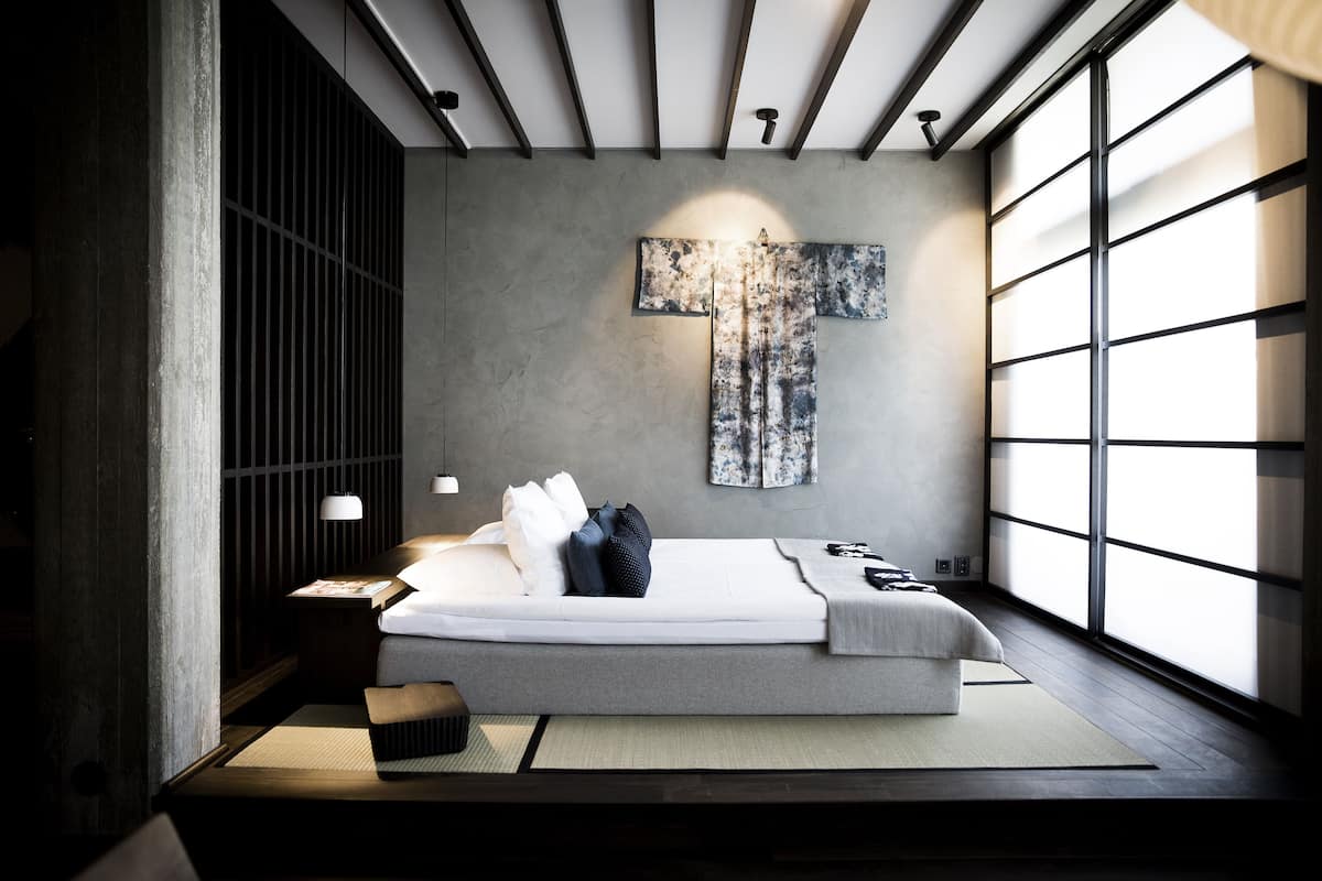 Un dormitorio moderno con una cama grande, un futón de tatami, una obra de arte en la pared y ventanas amplias.