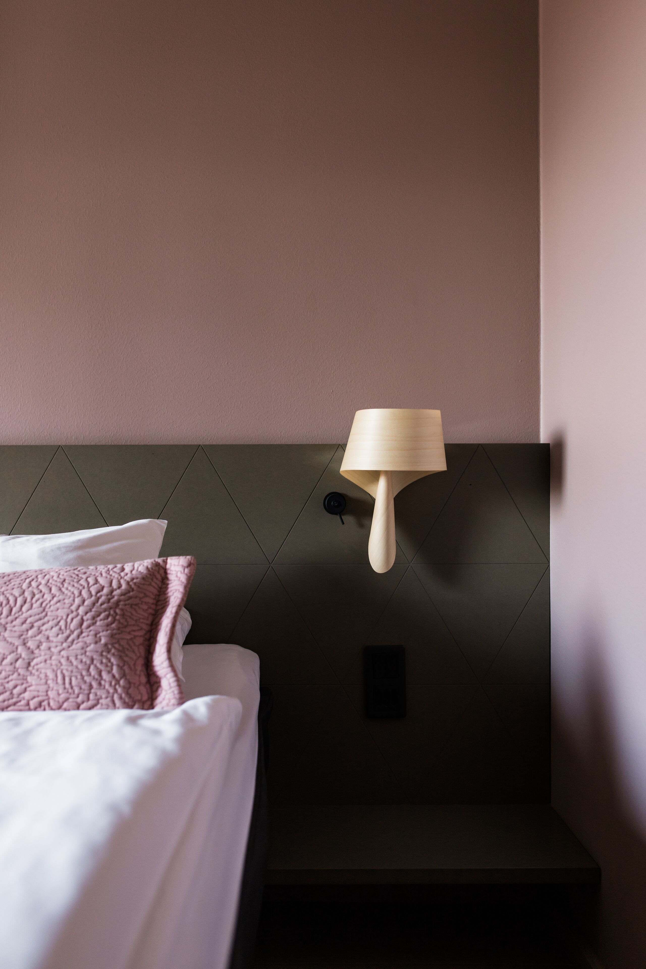 Una habitación de hotel con una cama, una lámpara de pared y un cabecero.