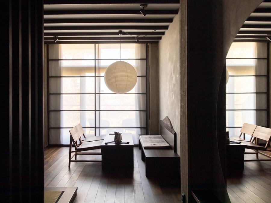 Una habitación minimalista con ventanas amplias, un farolillo de papel colgante y muebles de madera.