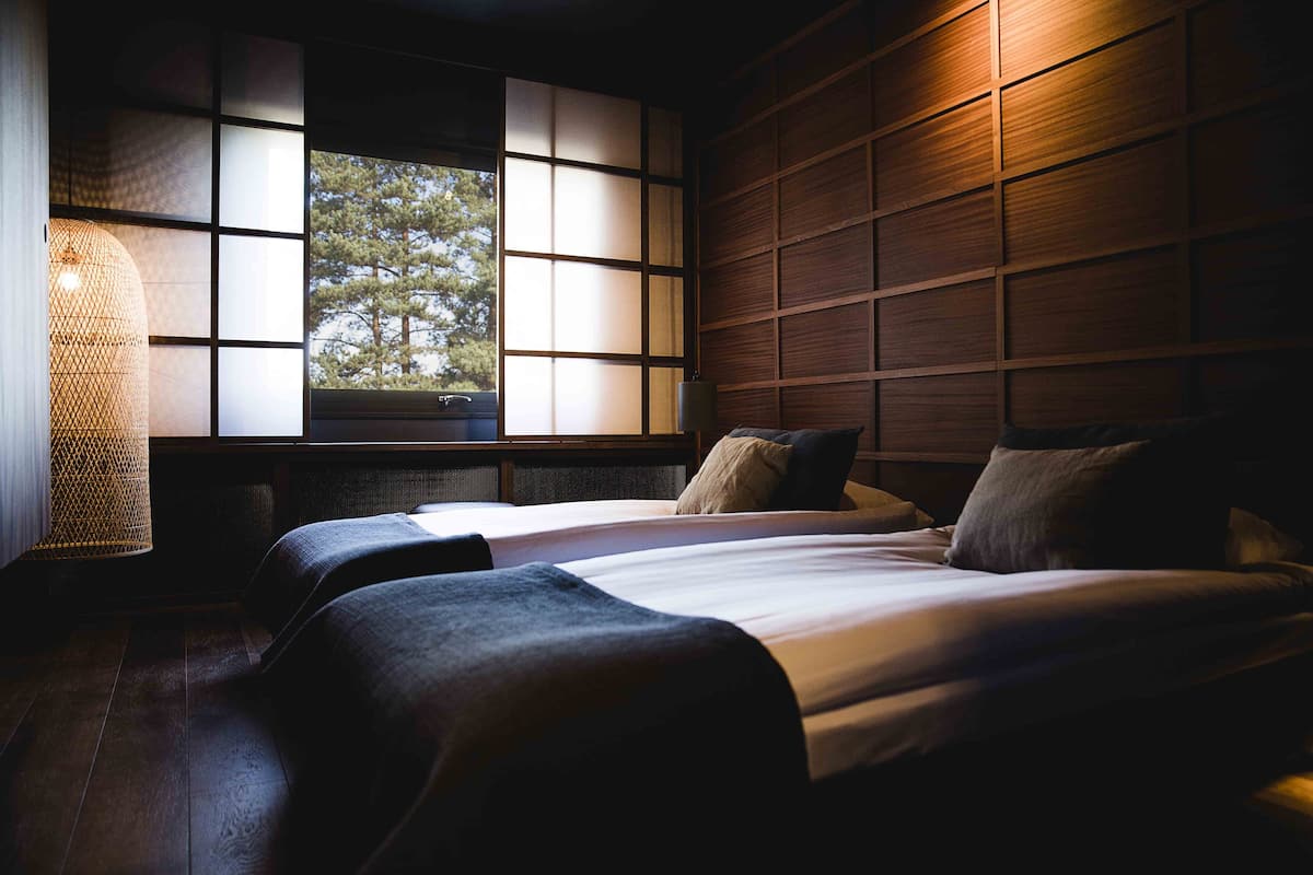 Un dormitorio con dos camas, un ventanal con vistas a árboles y paneles de madera en la pared.