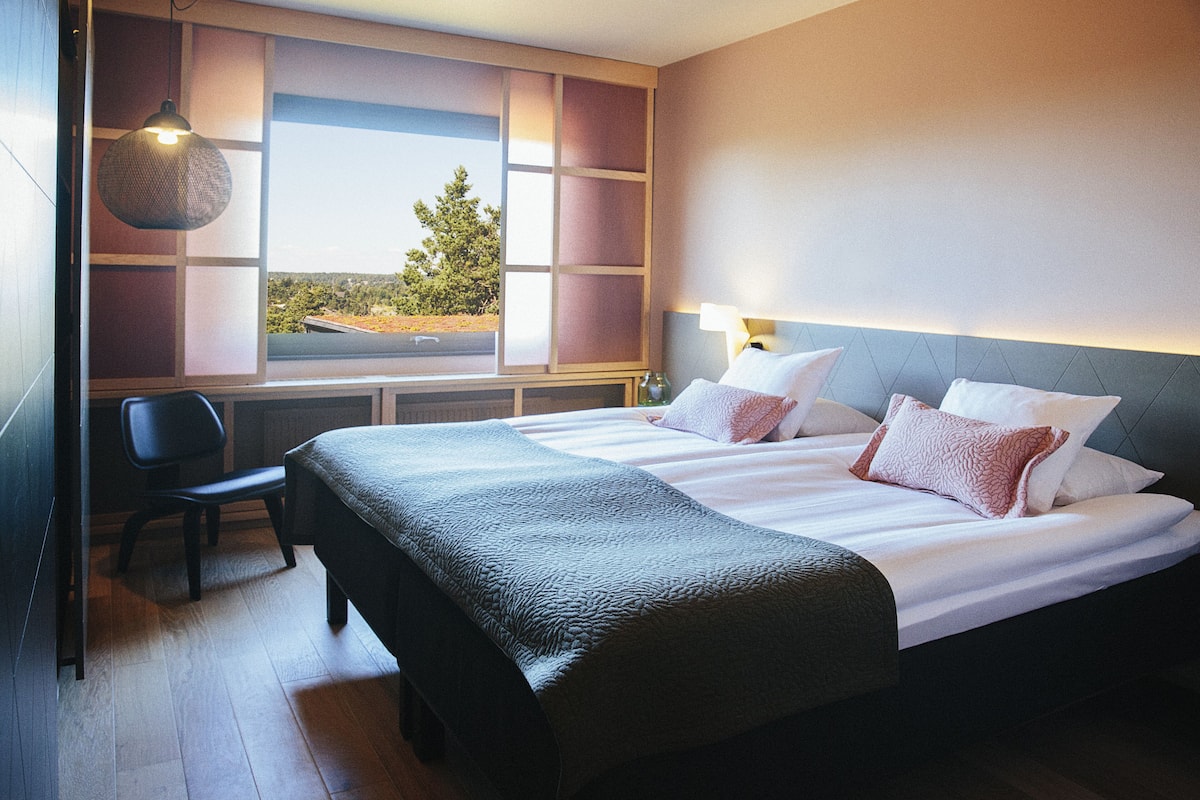 Habitación de hotel con una cama grande, una silla, una ventana con vistas y una lámpara colgante.