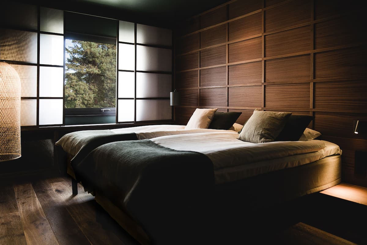 Un dormitorio con un ventanal grande, una cama con varias almohadas y paneles de madera en la pared.