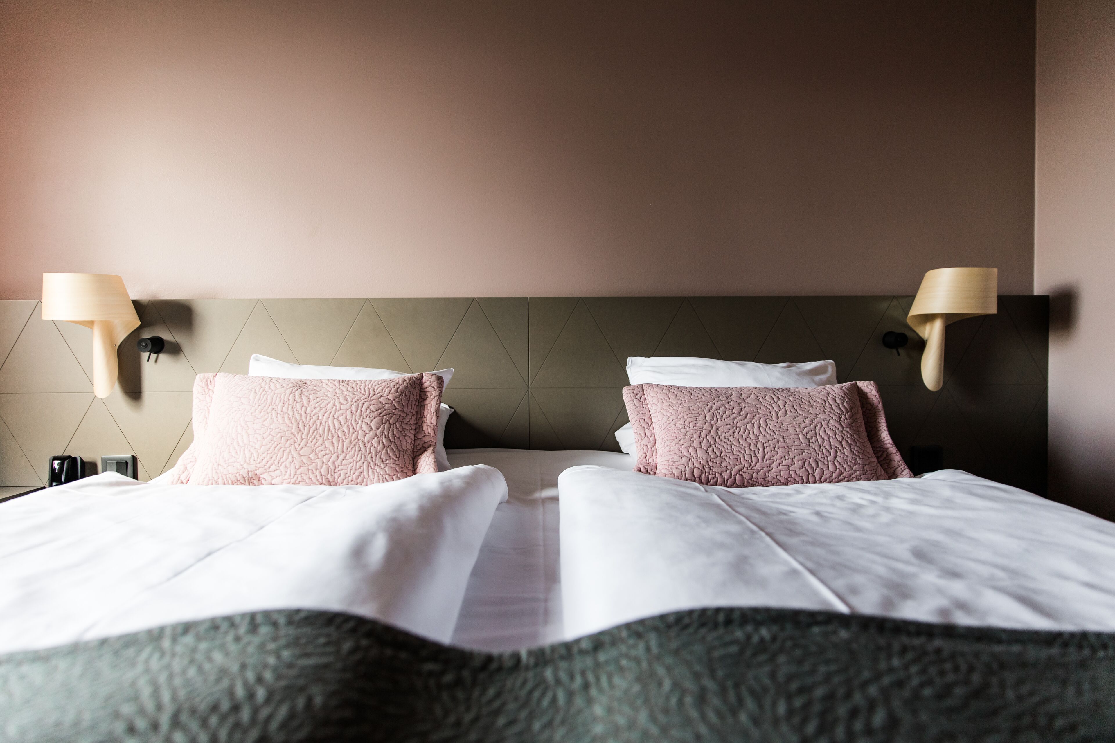 Una cama bien hecha con dos almohadas, un cabecero y dos lámparas fijadas a la pared.