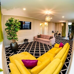 A modern living room with a sofa set, a large potted plant, and a flat-screen TV mounted on the wall. - Business V Hotel (Tirgu Mures)