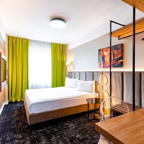 A hotel room with a bed, a desk, a chair, a painting, and a window with curtains. - Business V Hotel (Tirgu Mures)