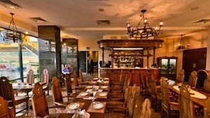 A restaurant with wooden tables and chairs, a bar area, and a view through large windows. - Business V Hotel (Tirgu Mures)