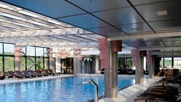 A large indoor swimming pool with clear glass walls, sun loungers, and a view of the outdoors. - Business V Hotel (Tirgu Mures)