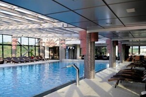 Una amplia piscina interior con paredes de vidrio transparente, tumbonas y vistas al exterior.