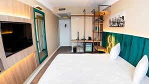 A hotel room with a large bed, a TV, a desk with a chair, and a cityscape picture on the wall. - Business V Hotel (Tirgu Mures)