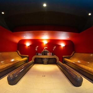 A spa room with red walls, two massage chairs, a reception desk, and wall-mounted lights. - Business V Hotel (Tirgu Mures)