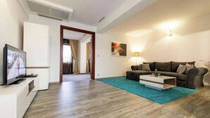 A modern living room with a flat-screen TV, a sofa, a coffee table, and a teal rug. - Business V Hotel (Tirgu Mures)