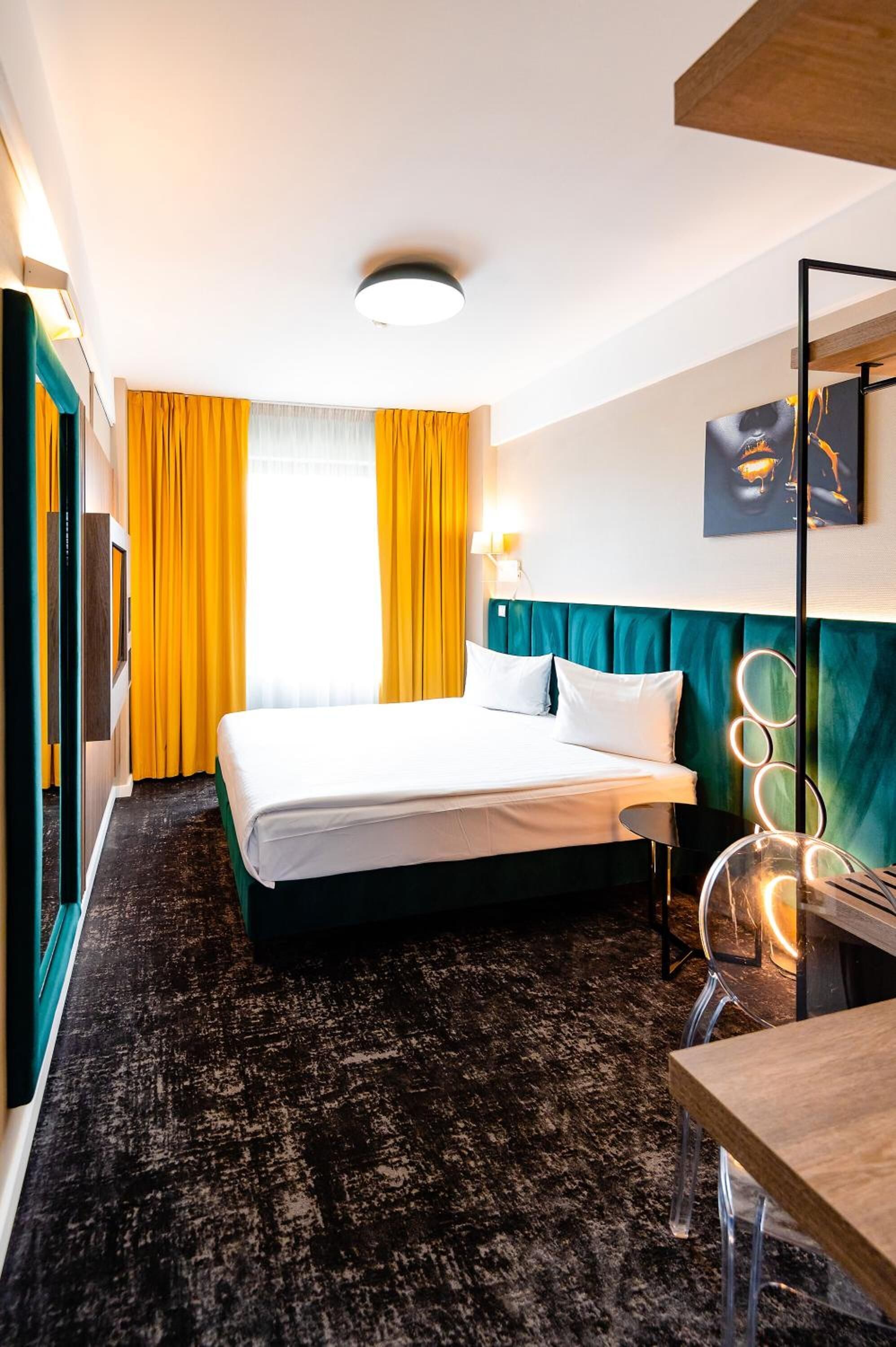 Ein Hotelzimmer mit einem Bett, einem Schreibtisch, einem Stuhl, einer Lampe und einem Bild an der Wand.