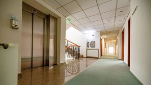 A hotel corridor with a carpeted floor, a water dispenser, an elevator, and a staircase.