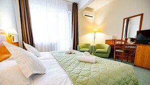 A hotel room with a bed, green armchair, desk, and a television.