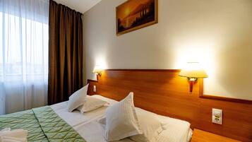 A hotel room with a large bed, two bedside lamps, a painting on the wall, and a window with curtains.