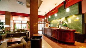 A hotel lobby with a reception desk, seating area, and a large window.